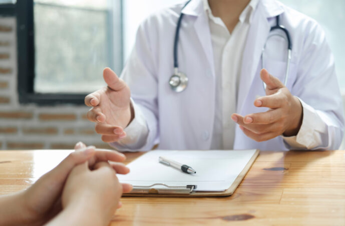 Doctor and patient. Close up of doctor explaining diagnosis and discussing treatment plans to patient with prescription in doctor office. Medical and health care concept.